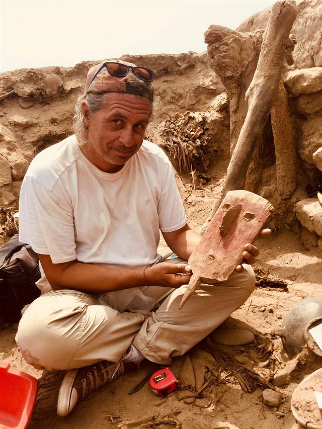 El arqueólogo Peter Eeckhout con una máscara de madera que estaba colocada sobre la cabeza de una momia que ya no se conserva porque fue saqueada. 