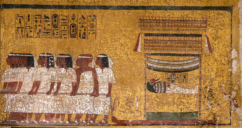 Muro este de la cámara funeraria de la tumba. Se muestra la momia de Tutankamón, acostada en un altar montado en un trineo, siendo dibujada por doce hombres en cinco grupos. Los hombres visten bandas blancas de luto sobre sus cejas. El último par, distinguido por sus cabezas afeitadas y su vestimenta diferente, son los dos visires del Alto y Bajo Egipto